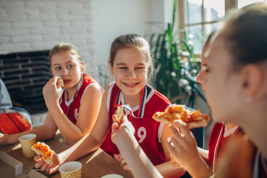 Kids on a sports team eating pizza together while celebrating